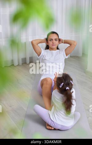 Mutter macht Crunches auf einer Yogamatte, während ihre Tochter in der Nähe beobachtet Stockfoto