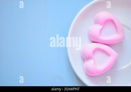 Souffle Dessert, französisches Souffle Konzept. Zwei herzförmige pinkfarbene Souffle-Kuchen liegen auf dem weißen Porzellanteller auf dem blauen Holztisch, romantischer bre Stockfoto