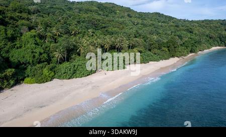 Atemberaubender Blick aus der Vogelperspektive auf einen unberührten Sandstrand, der auf das klare, lebhafte türkisfarbene und tiefblaue Meer trifft. Stockfoto
