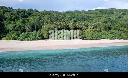 Atemberaubender Blick aus der Vogelperspektive auf einen unberührten Sandstrand, der auf das klare, lebhafte türkisfarbene und tiefblaue Meer trifft. Stockfoto