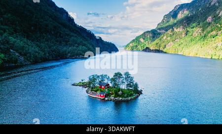 Lovrafjorden bietet einen atemberaubenden Blick auf eine bezaubernde rote Hütte auf einer winzigen Insel, umgeben von ruhigem Wasser und üppigen Bergen. Stockfoto