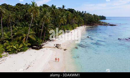Weiße Sandstrände treffen auf klares türkisfarbenes Wasser auf Koh Kood Island. Zwei Personen schlendern am Strand unter einem hellblauen Himmel entlang, umgeben von hohen Palmen und tropischem Grün in Thailand || Model veröffentlicht Stockfoto