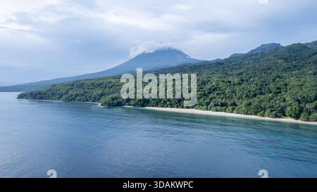 Weite Luftaufnahme einer tropischen Inselküste mit abgeschiedenem Sandstrand, tiefblauem Ozean, üppigem Wald und Inerie-Vulkan. Stockfoto