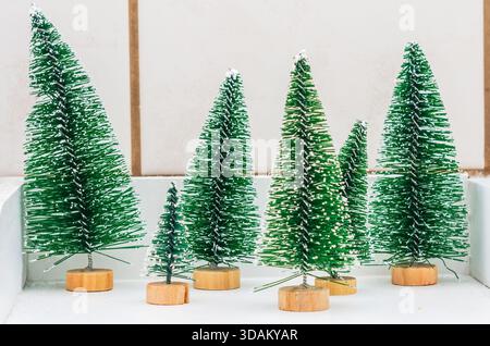 Sortiment an künstlichen Miniaturbäumen mit beflockten weißen Spitzen auf Holzsockel Stockfoto