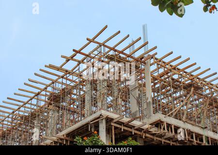Umfangreiches Holzgerüst, das den Stahlbetonrahmen in den oberen Geschossen eines im Bau befindlichen Gebäudes mit Laub umgibt. Stockfoto
