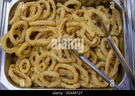 Eine großzügige Portion frittierter Calamari-Ringe, die mit einem leichten Teig überzogen und zu einem perfekten goldgelben Crisp gekocht sind, werden in einem Edelstahl-Tra präsentiert Stockfoto
