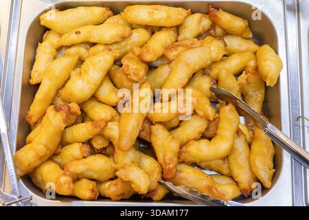 Eine große Menge goldbrauner, knuspriger Fischfinger, die hoch in einem Serviertablett aus Edelstahl gestapelt sind und bereit sind Stockfoto