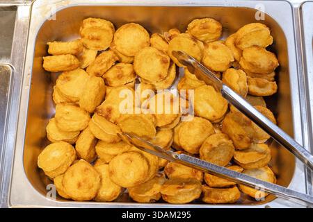 Aus nächster Nähe sehen Sie ein großes Metalltablett, das mit zahlreichen goldbraunen, runden, frittierten Fischkuchen gefüllt ist und servierfertig ist Stockfoto