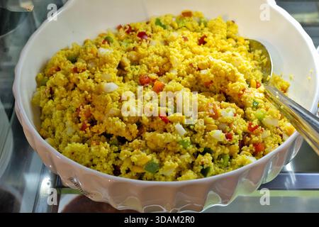 Ein lebendiger und nahrhafter Couscous-Salat wird in einer großen weißen Servierschale mit fein gehackten Paprika, Zwiebeln und Maiskernen serviert. Stockfoto