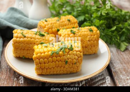 Stücke gekochter Maiskolben mit Petersilie auf Holztisch, Großaufnahme Stockfoto