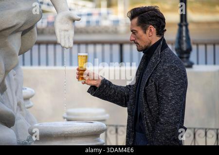 London, Großbritannien. Dezember 2025. Das englische Model David Gandy schaut sich sein Bier während der Dreharbeiten im Londoner South Bank an. Premium-Bier, Peroni Nastro Azzurro, Großbritanniens beliebtestes Bier, stellte am Aussichtspunkt in South Bank, London das La Fontana di Azzurro „Water into Beer“ des englischen Modells David Gandy vor. Der Anlass wird vom 10. Bis 14. Dezember 2025 für die Öffentlichkeit geöffnet sein, um die Feiertage in der Nation anzufeuern. Quelle: SOPA Images Limited/Alamy Live News Stockfoto