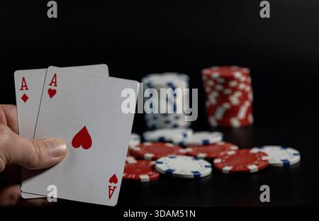 Person mit Spielkarten, die ein Paar Asse mit Casino-Chips auf einem dunklen Tisch zeigen Stockfoto
