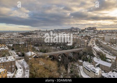 Aus der Vogelperspektive auf eine schneebedeckte Stadt, die sich unter einem stimmungsvollen Himmel ausbreitet, das berühmte Edinburgh Castle auf einem fernen Hügel thront, ein Zeugnis der Geschichte und Geschichte Stockfoto