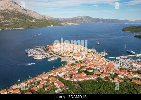 Blick aus der Vogelperspektive auf die faszinierende Inselstadt mit ihren Terrakotta-Dächern, die in Richtung azurblaues Meer kaskadieren, eingerahmt von zerklüfteten Bergen, Korcula, Dubrovni Stockfoto