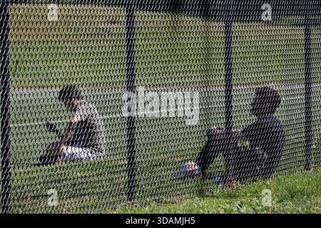 Väter sitzen hinter einem Zaun und beobachten ihre Kinder Fußball auf einem Spielfeld. Stockfoto