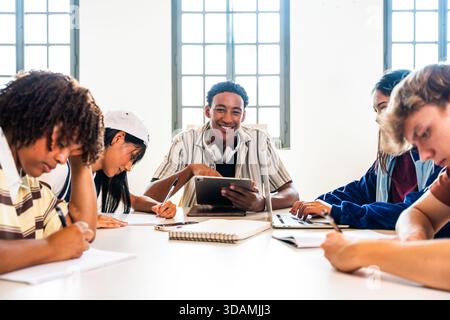 Multiethnische Gruppe junger Studenten, die sich in der Bibliothek treffen - junge multiethnische Studenten lächeln und gemeinsam in einer Universitätsbibliothek mit Lasche studieren Stockfoto