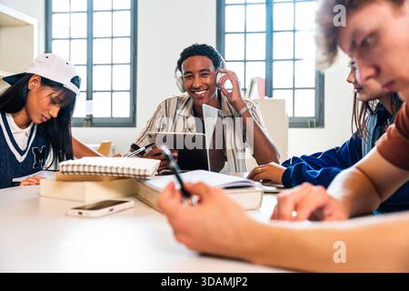 Multiethnische Gruppe junger Studenten, die sich in der Bibliothek treffen - vielfältige Gruppe junger Studenten, die an einem Bibliothekstisch zusammenarbeiten und lernen, mit Hilfe von digi Stockfoto