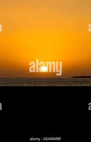 Blick auf den Sonnenuntergang über dem ruhigen Wasser, der lange Schatten und warme Farbtöne über die Szene wirft, Karachi, Sindh, Pakistan. Stockfoto