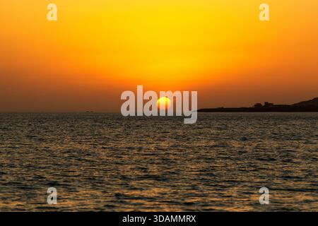 Blick auf einen brillanten Sonnenuntergang, der ein goldenes Leuchten über das ruhige Meer wirft, mit einer fernen Landmasse, die sich vor dem pulsierenden Horizont Karachi, Sind befindet Stockfoto