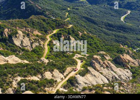 Serpentine, unbefestigte Straße führt durch die zerklüfteten Hügel von Calabasas, mit sonnendurchfluteten Felsformationen, leuchtendem Grün und weit entfernten Bergen unter einer Brille Stockfoto