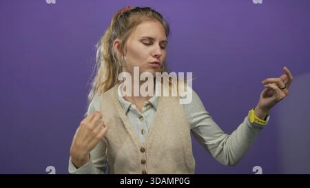 Die Frau benutzt Hände, die im Studio eine Luftgitarre umhauen und zeigt einen blonden jungen Darsteller vor einer violetten Wand, die Haare, Ohrringe und Weste hervorhebt. Stockfoto