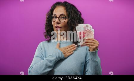 Frau, die isländische Kronen-Banknoten vor einem leuchtend violetten Hintergrund hält und damit finanzielle Verpflichtungen oder Versprechen symbolisiert. Stockfoto