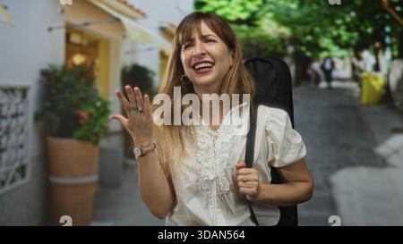 Frau singt mit Gitarrenhülle auf dem Rücken, Hand in ausdrucksvoller Geste auf der Straße angehoben; Freude Musik Reise. Stockfoto