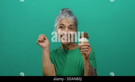 Frau, die mit Eis vor einem leuchtend grünen Hintergrund feiert und Freude und köstliche Genüsse in einer isolierten Umgebung präsentiert, in grünem Shi Stockfoto