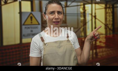 Frau zeigt mit dem Finger auf Baugerüste, die mit orangefarbenem Sicherheitsnetz auf einer Baustelle im Freien bedeckt sind; Sicherheitshinweise Warnung Vorsicht. Stockfoto