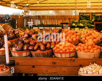 Frische Auberginen, Tomaten und Gemüse der Saison werden in Holzkörben auf einem Bauernmarkt im Freien bei warmem Tageslicht präsentiert. Stockfoto
