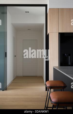 Innenausstattung eines modernen und stilvollen Apartments. Die Aussicht zeigt einen Flur mit hellem Holzfußboden und minimalistischen weißen Türen mit schwarzen Griffen. In der Zukunft Stockfoto