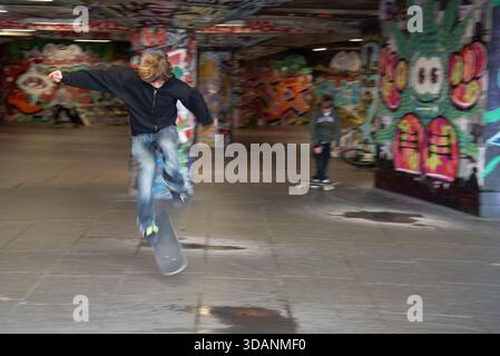 Junge Skateboarder springen mit Bewegungsunschärfe in einem lebendigen urbanen Skatepark an Bord Stockfoto