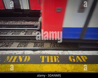 Gelber Hinweis auf den Lückentext auf einem londoner U-Bahn-Bahnsteig mit dem sich nähernden Zug. Warnschild der U-Bahn-Station Stockfoto