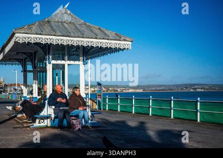 Im Dezember entspannen sich die Menschen in einem historischen viktorianischen Küstenschutz an der Weymouth Promenade bei Wintersonne. Stockfoto