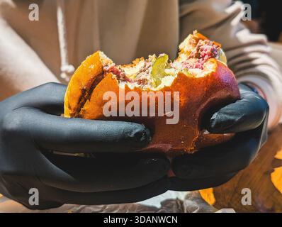 Hände in schwarzen Handschuhen, die halb gegessen Gourmet-Rindfleisch-Burger halten Stockfoto