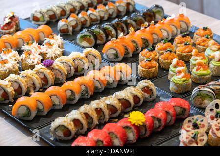 Eine lebendige Auswahl an verschiedenen Arten von Gourmet-Sushi und Maki-Rollen mit verschiedenen Geschmacksrichtungen und künstlerischen Darstellungen ist auf schwarzem Pl angeordnet Stockfoto