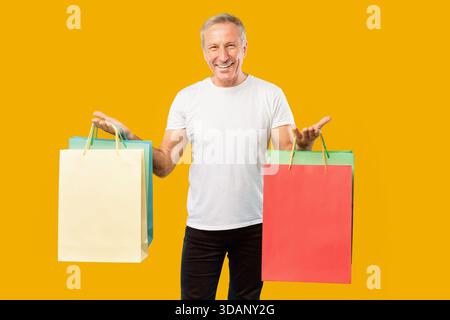 Der 65-jährige Mann lächelt und hält bunte Einkaufstaschen in einer hellen Umgebung Stockfoto