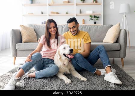 Das Paar genießt einen freudigen Moment mit Golden Retriever im gemütlichen Wohnzimmer am sonnigen Nachmittag Stockfoto