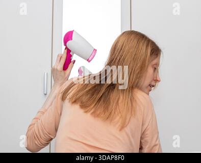 Junge Frau trocknet Haare mit Haartrockner zu Hause vor einem Spiegel Stockfoto