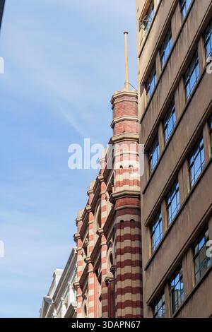 Ein flaches urbanes Bild, das die unterschiedlichen Stile eines historischen roten Backsteingebäudes und einer modernen braunen Fassade unter einem klaren blauen Himmel festlegt. Stockfoto
