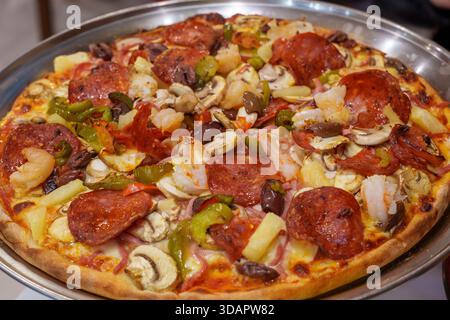 Eine große, frisch gebackene Pizza wird auf einem Metalltablett präsentiert, das großzügig mit verschiedenen bunten und appetitlichen Belägen bedeckt ist. Stockfoto