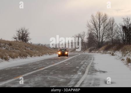 Ein warmes Fahrzeug fährt über eine schneebedeckte Straße im Ludington State Park, während die ruhige Winterlandschaft von Schönheit umgeben ist. Stockfoto