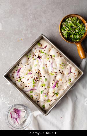 Draufsicht von Zwiebeln- und Schalottenfokaccia-Teigscheiben in einer quadratischen Backform, Draufsicht von luftiger, sprudelnder Zwiebelfokaccia-Teigprobung Stockfoto