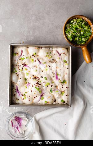 Draufsicht von Zwiebeln- und Schalottenfokaccia-Teigscheiben in einer quadratischen Backform, Draufsicht von luftiger, sprudelnder Zwiebelfokaccia-Teigprobung Stockfoto