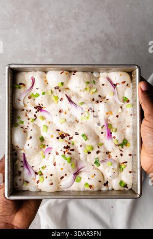 Draufsicht von Zwiebeln- und Schalottenfokaccia-Teigscheiben in einer quadratischen Backform, Draufsicht von luftiger, sprudelnder Zwiebelfokaccia-Teigprobung Stockfoto