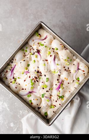 Draufsicht von Zwiebeln- und Schalottenfokaccia-Teigscheiben in einer quadratischen Backform, Draufsicht von luftiger, sprudelnder Zwiebelfokaccia-Teigprobung Stockfoto