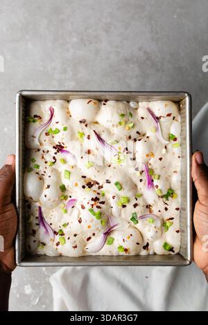 Draufsicht von Zwiebeln- und Schalottenfokaccia-Teigscheiben in einer quadratischen Backform, Draufsicht von luftiger, sprudelnder Zwiebelfokaccia-Teigprobung Stockfoto