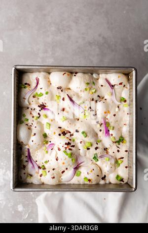 Draufsicht von Zwiebeln- und Schalottenfokaccia-Teigscheiben in einer quadratischen Backform, Draufsicht von luftiger, sprudelnder Zwiebelfokaccia-Teigprobung Stockfoto