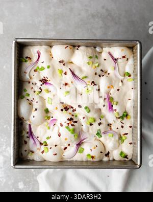 Draufsicht von Zwiebeln- und Schalottenfokaccia-Teigscheiben in einer quadratischen Backform, Draufsicht von luftiger, sprudelnder Zwiebelfokaccia-Teigprobung Stockfoto