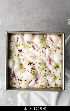 Draufsicht von Zwiebeln- und Schalottenfokaccia-Teigscheiben in einer quadratischen Backform, Draufsicht von luftiger, sprudelnder Zwiebelfokaccia-Teigprobung Stockfoto